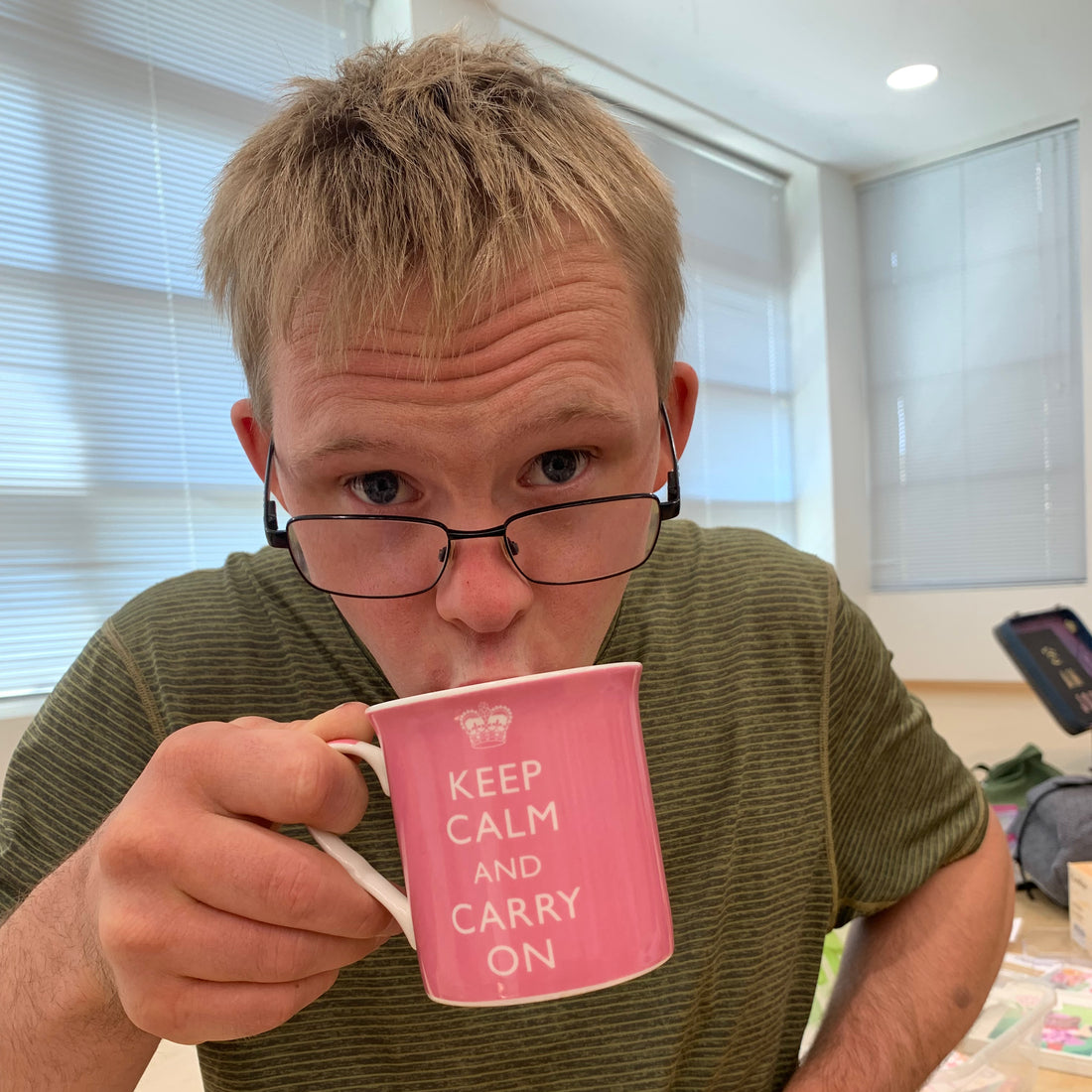 man in green shirt drink from a mug that reads "keep calm and carry on"