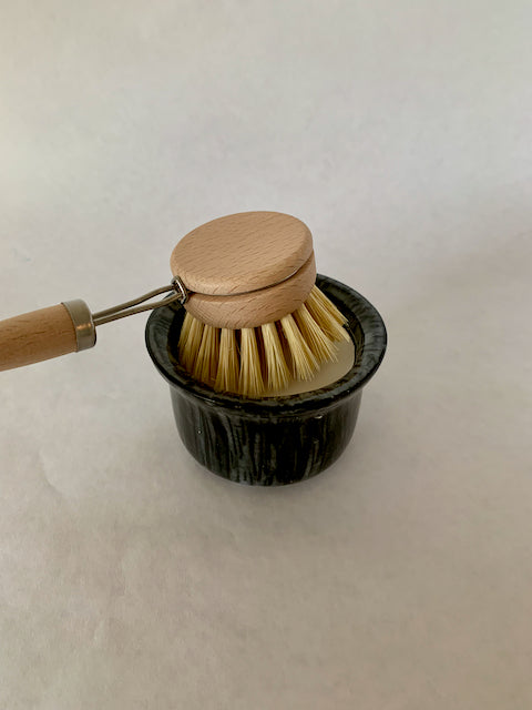 wood dish brush resting on white soap in a black ramekin