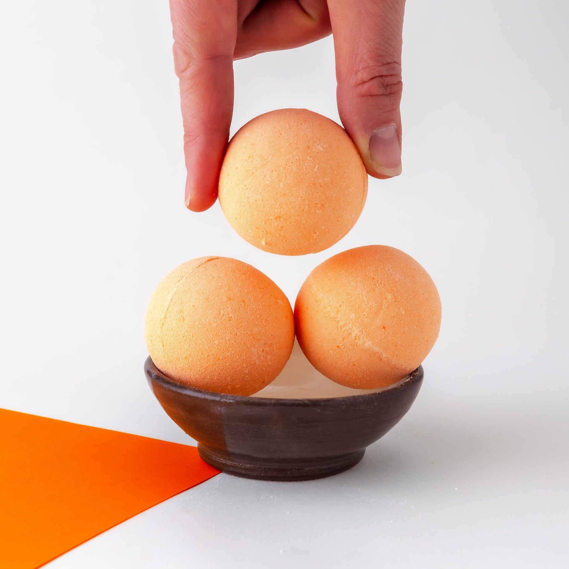 three orange bath bombs, one held by a thumb and finger