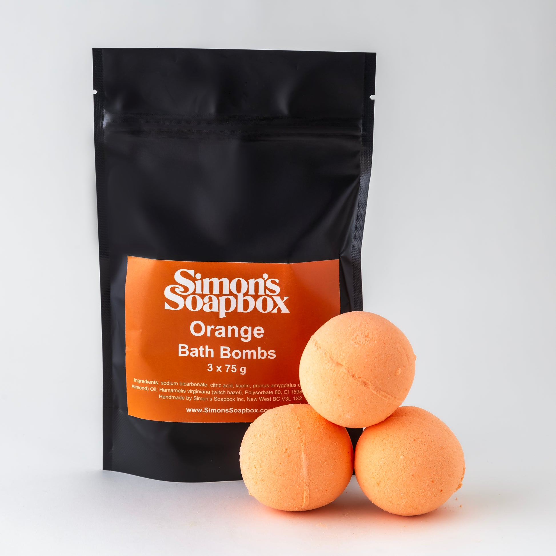 three orange round bath bombs in front of black stand up pouch