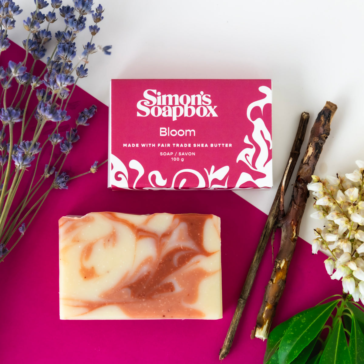 unpackaged bar of soap beside packaged bar of soap, bark, lavender and white flowers