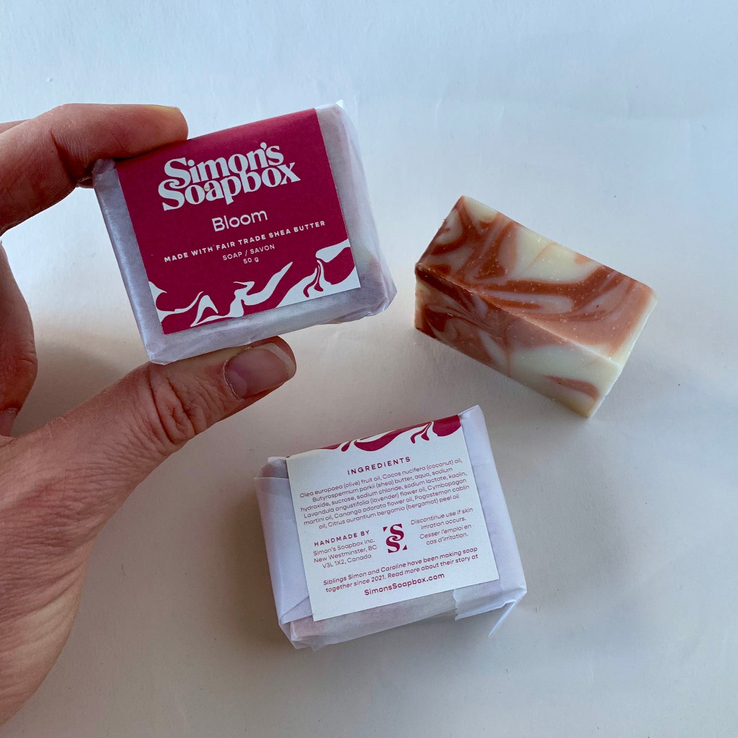 Hand holding a bar of Simon's Soapbox soap with packaging on a white background