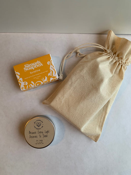 yellow package of bar soap and silver tin beside a cream cotton drawstring bag
