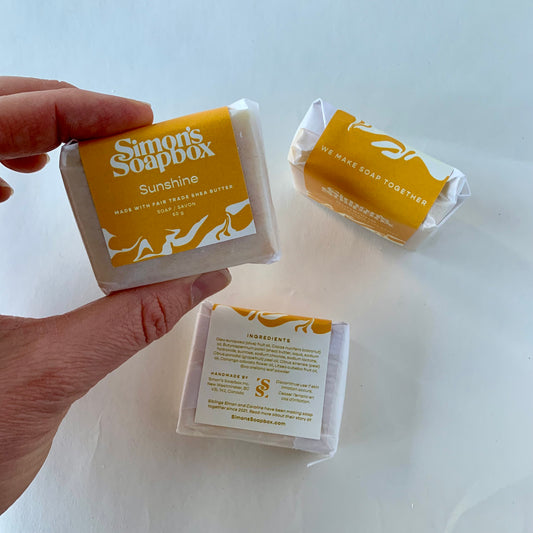 Hand holding a bar of soap with 'Simon's Soapbox' branding on a white background
