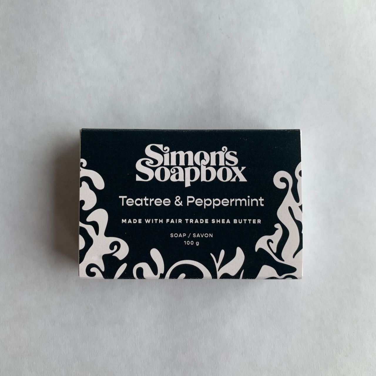rectangle package black with white swirl design and text Simon's Soapbox Tea Tree and Peppermint made with fair trade shea butter soap/savon 100 g