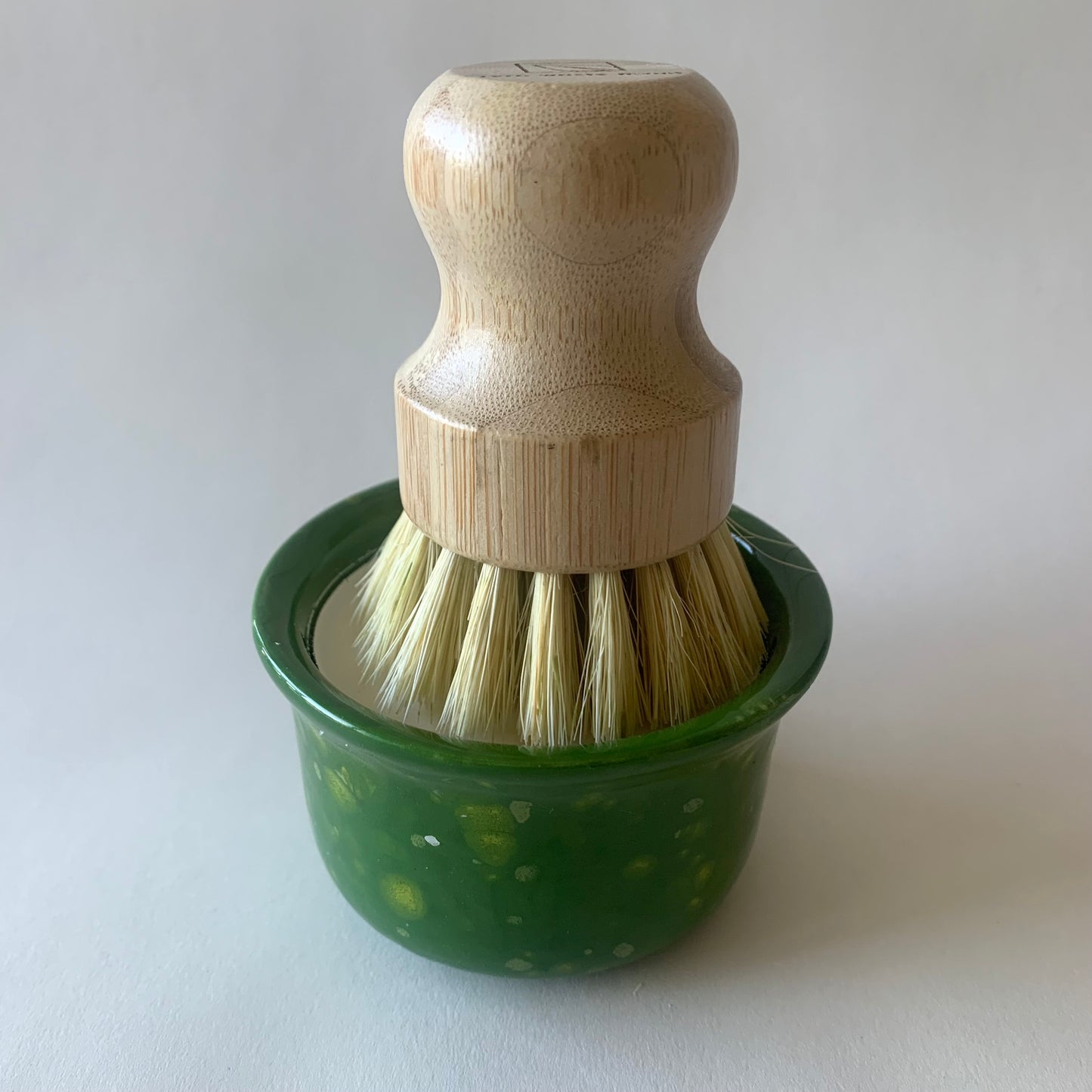 green ramekin with wood dish brush resting on soap