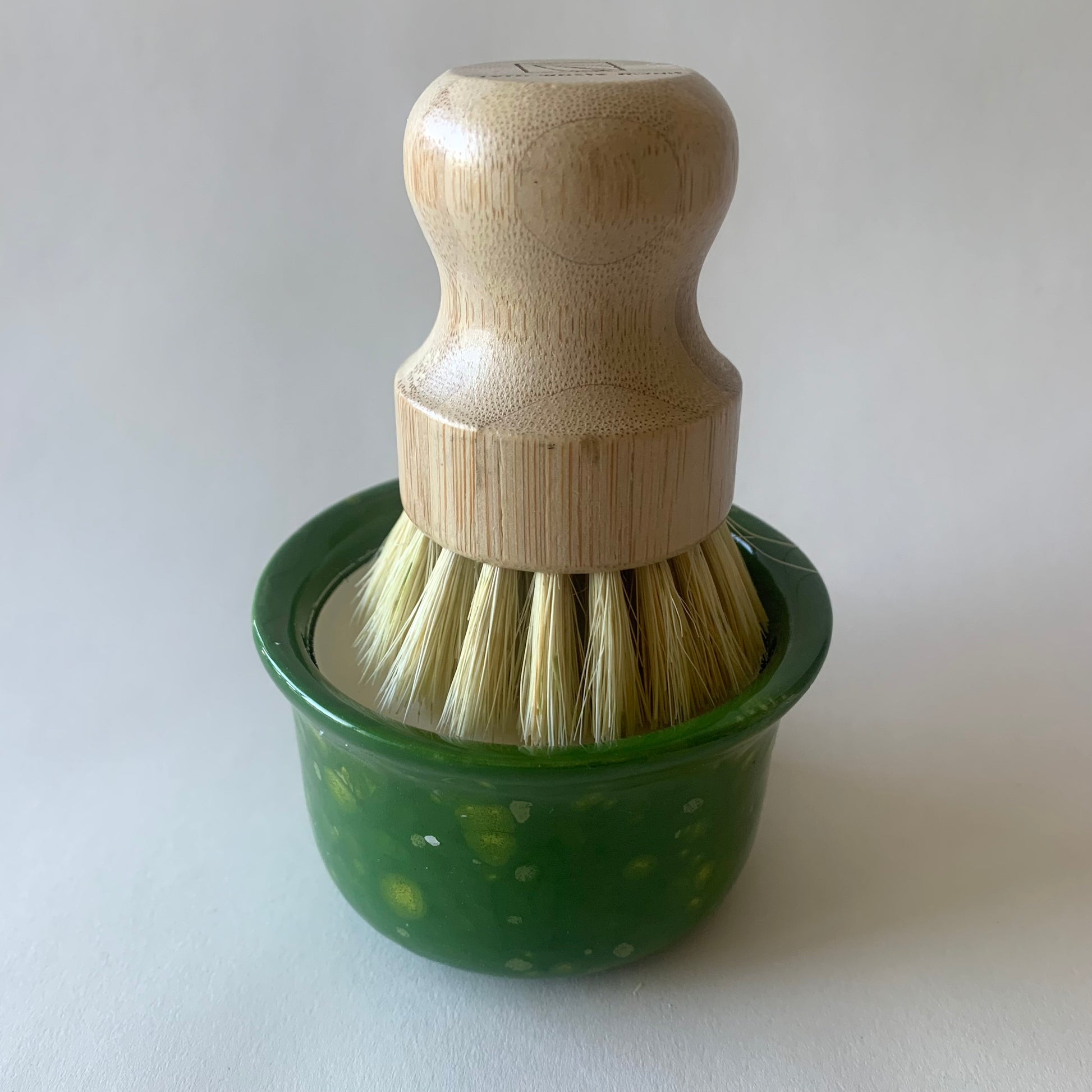 green ramekin with wood dish brush resting on soap
